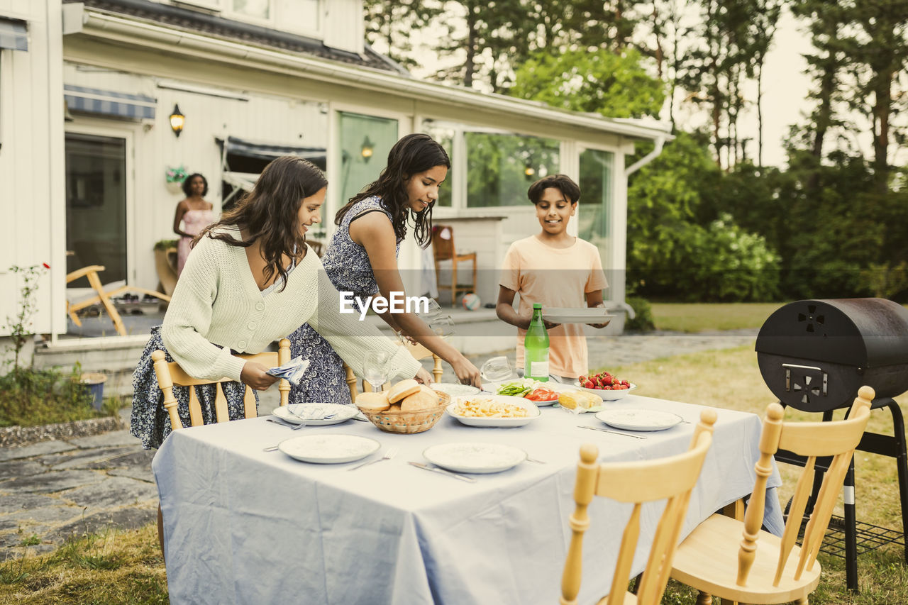 Siblings setting up food on table in back yard