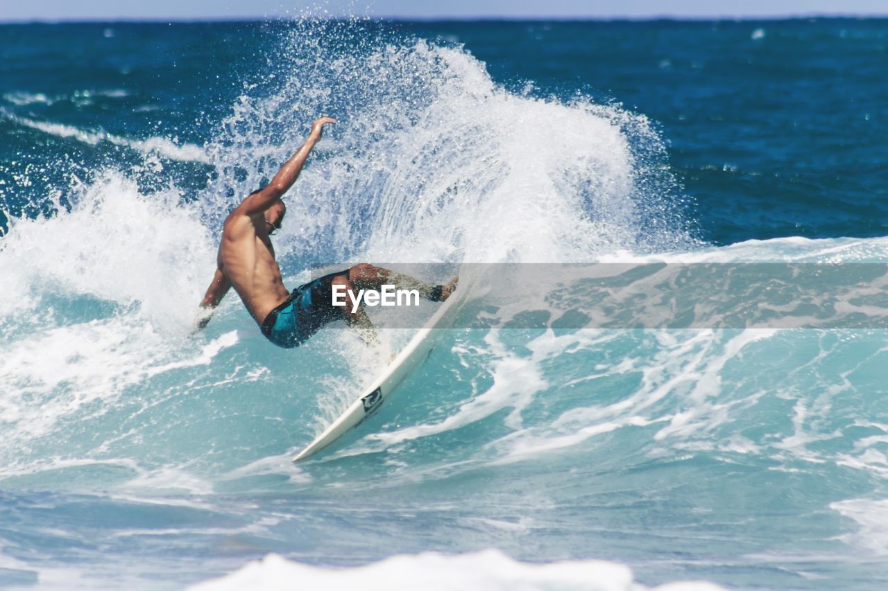 Shirtless man surfing in sea