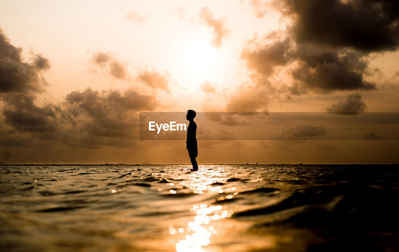 Silhouette man standing on beach against sky during sunset