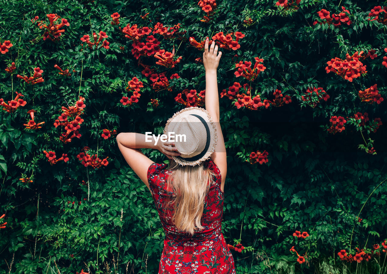 Rear view of woman standing by red flowering plant