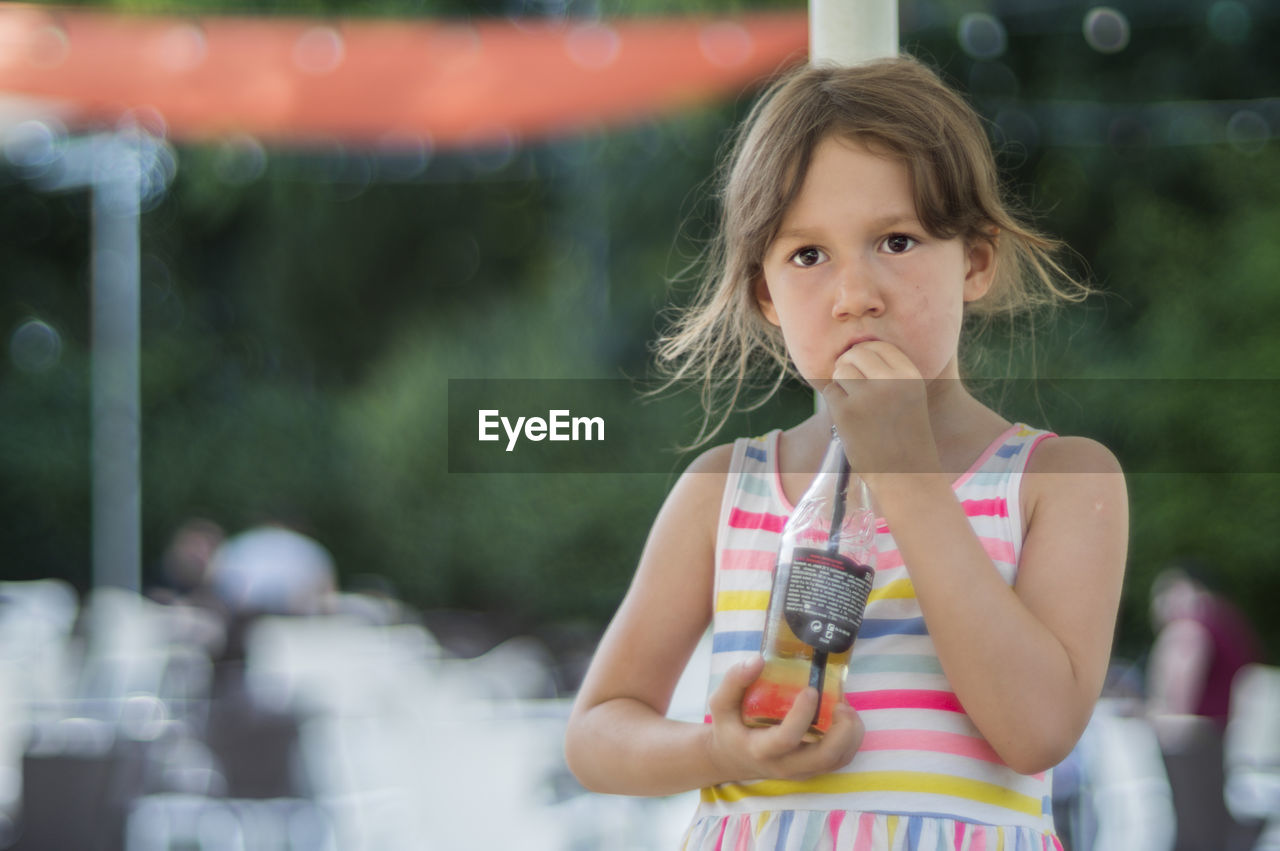 Girl drinking cold drink from bottle while standing at outdoor cafe