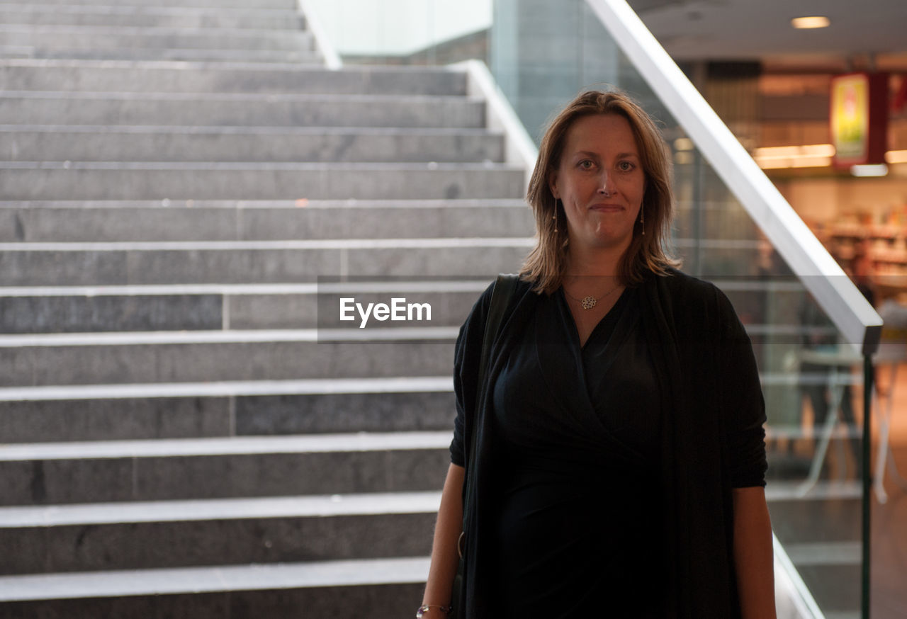 Portrait of woman standing against staircase