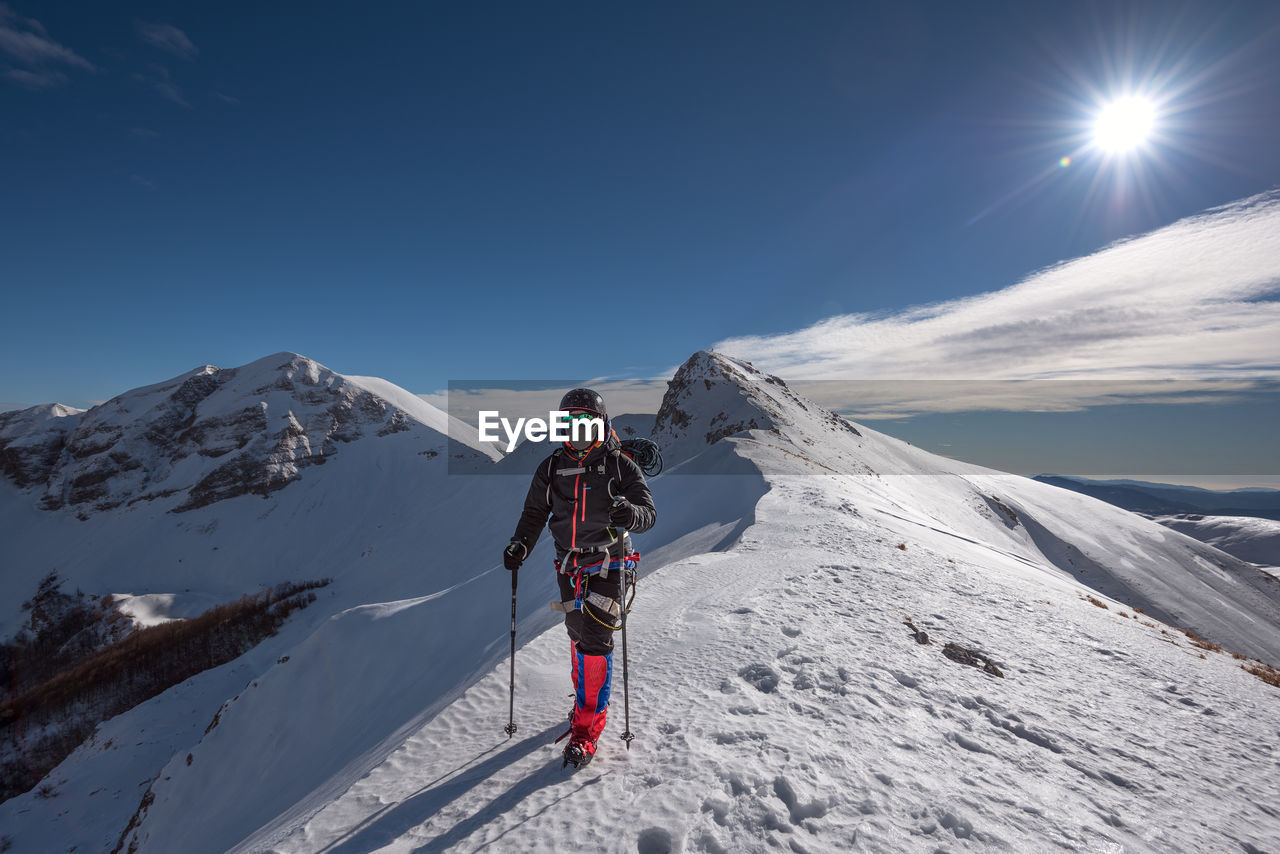 Man climbing on snowcapped mountain against sky