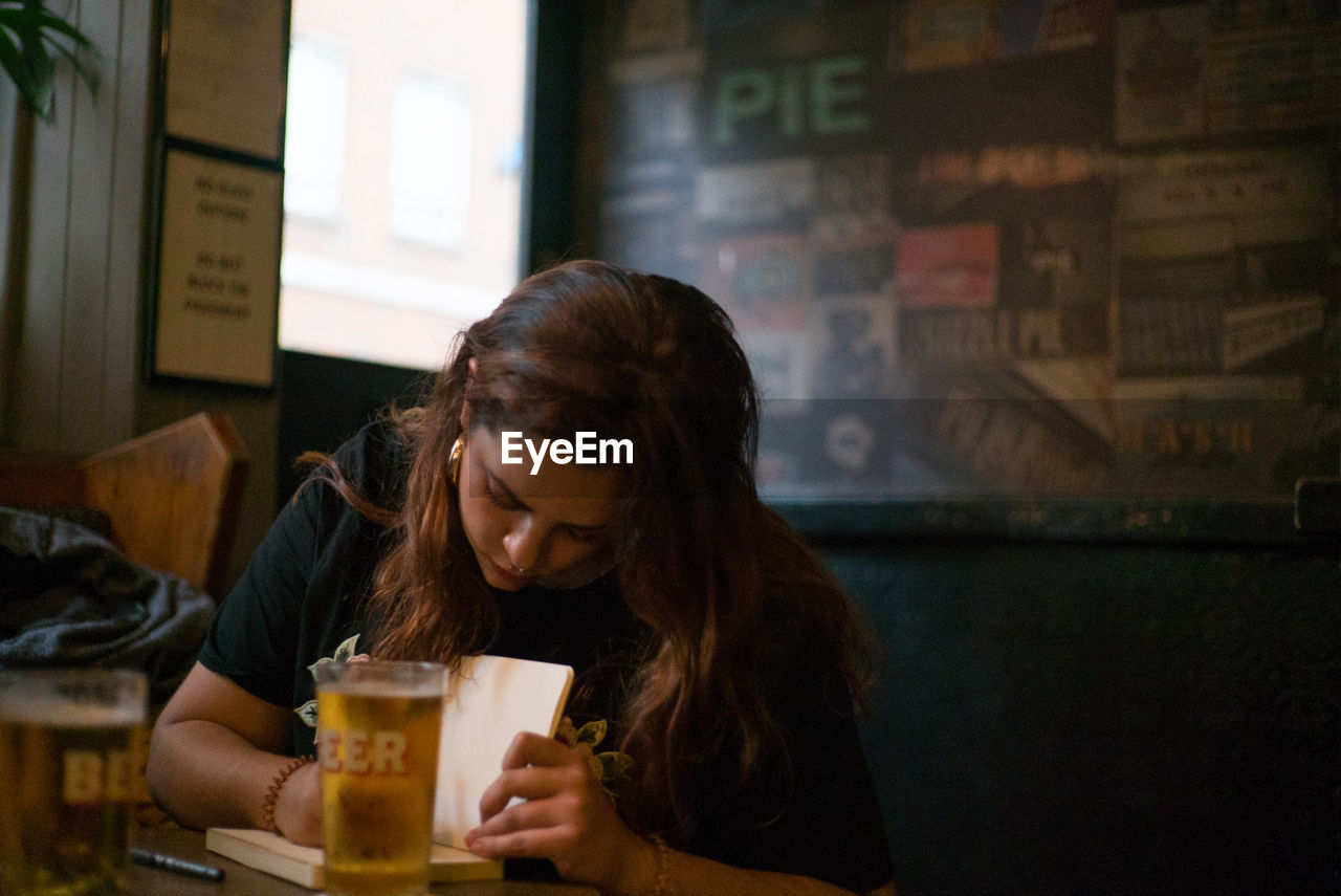 YOUNG WOMAN DRINKING GLASS ON TABLE AT CAFE