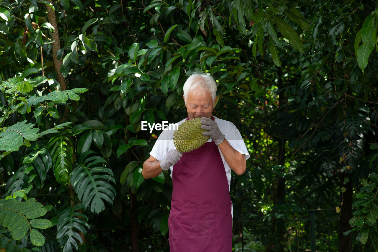 Man examining durian while standing against trees