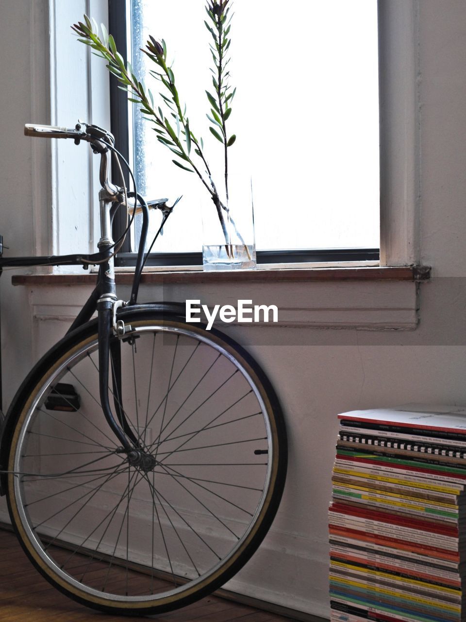 Bicycle parked safely inside house next to stack of book against window wall