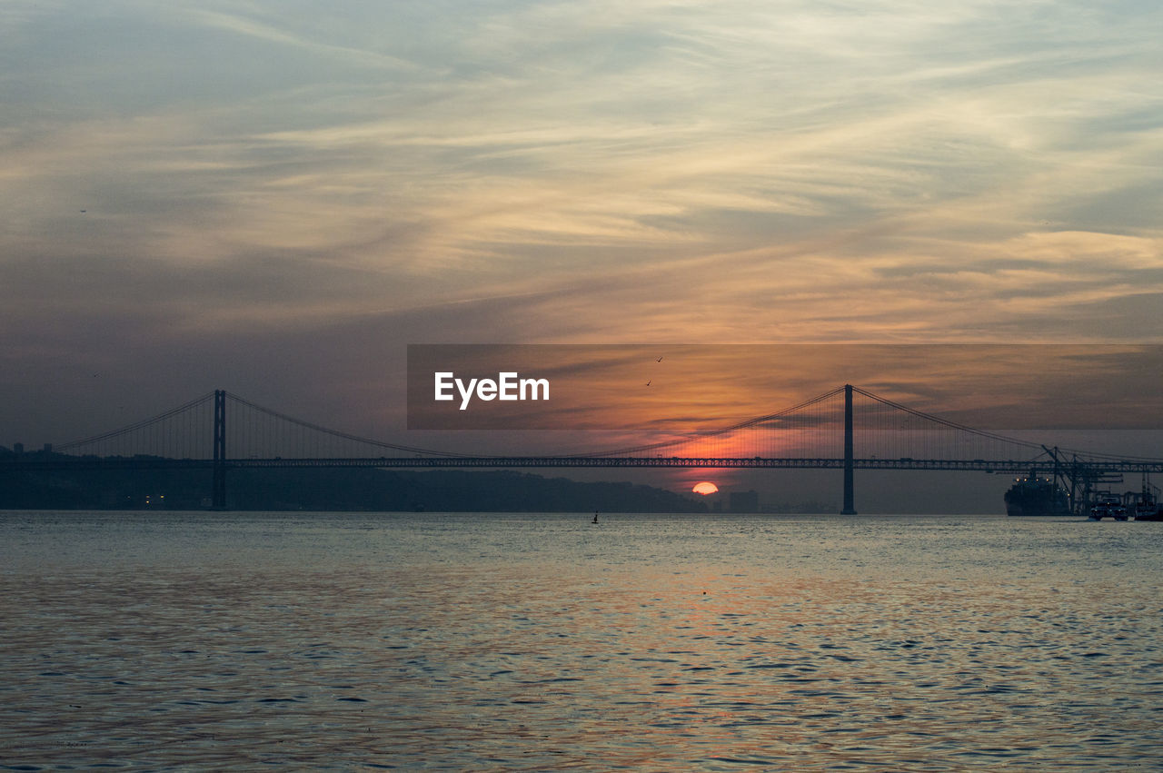 Suspension bridge over sea against sky during sunset