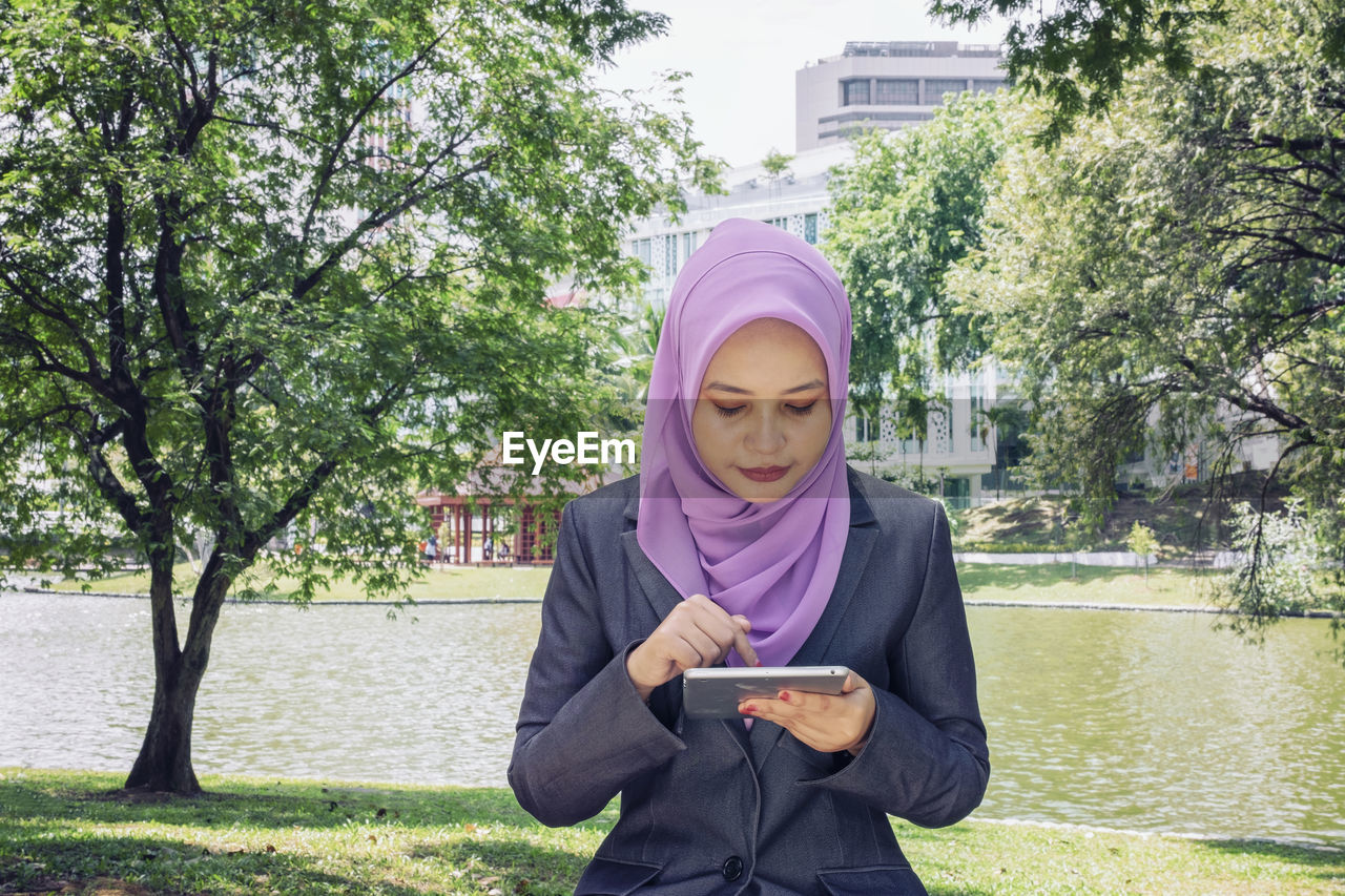  young woman with hijab sitting and texting her friends using her handphone