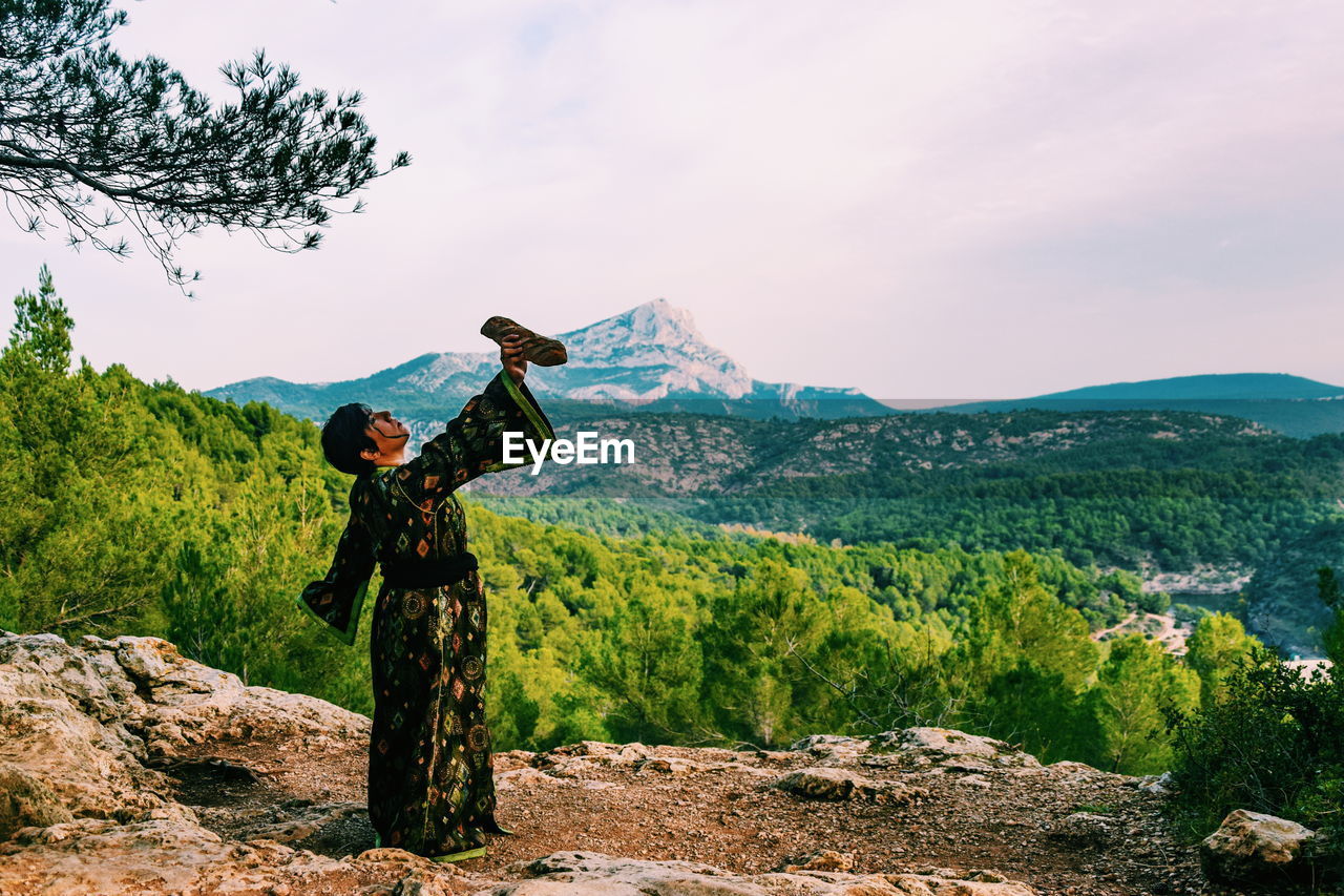 Woman with arms raised on mountain against sky