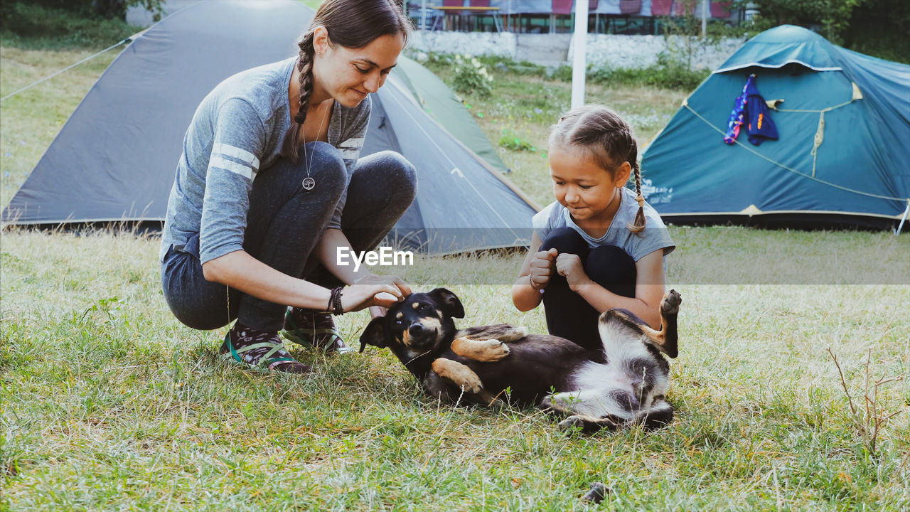 Mother and daughter playing dog on grassy land