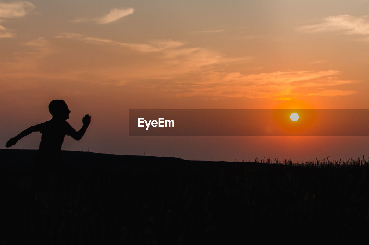 Silhouette boy running on field against orange sky during sunset