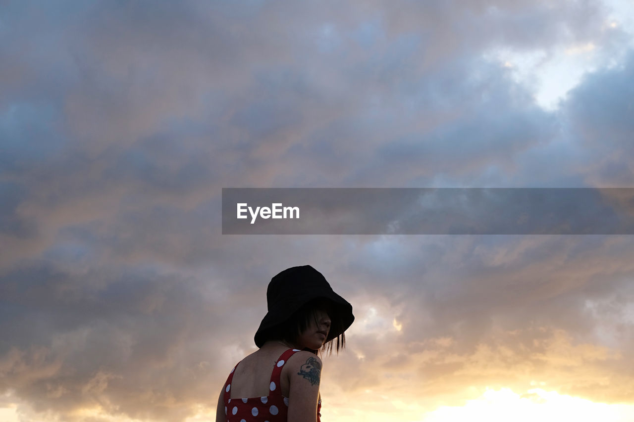 sky, cloud, sunset, one person, nature, hat, sunlight, child, childhood, sun hat, clothing, adult, standing, horizon, outdoors, looking, women, silhouette, beauty in nature, waist up, copy space, evening, lifestyles, leisure activity, person, dramatic sky, back lit, female, low angle view, fashion accessory, emotion, dusk, casual clothing