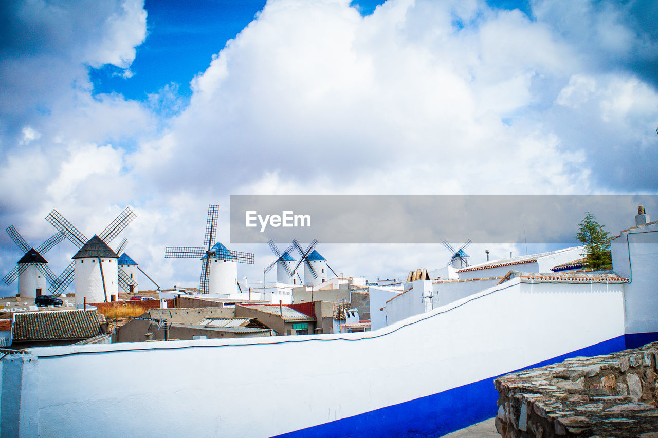 Buildings and windmills against cloudy sky