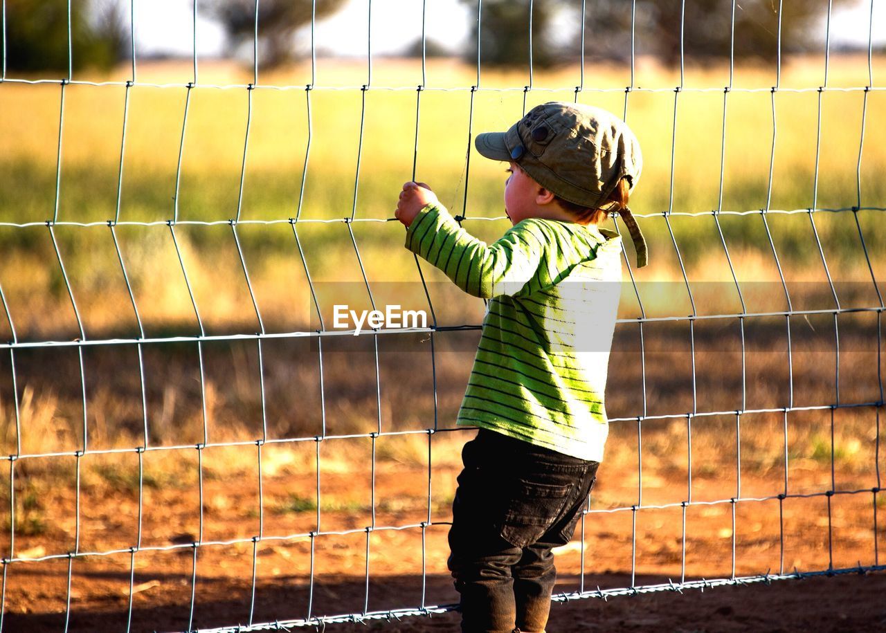 Rear view of baby boy holding fence on field