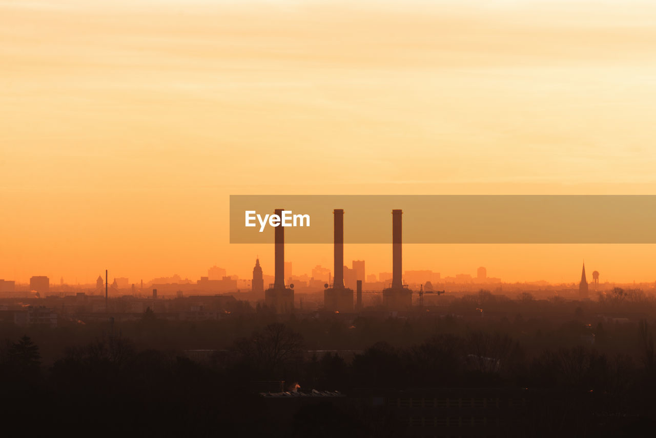 Silhouette factories in city against sky during sunset