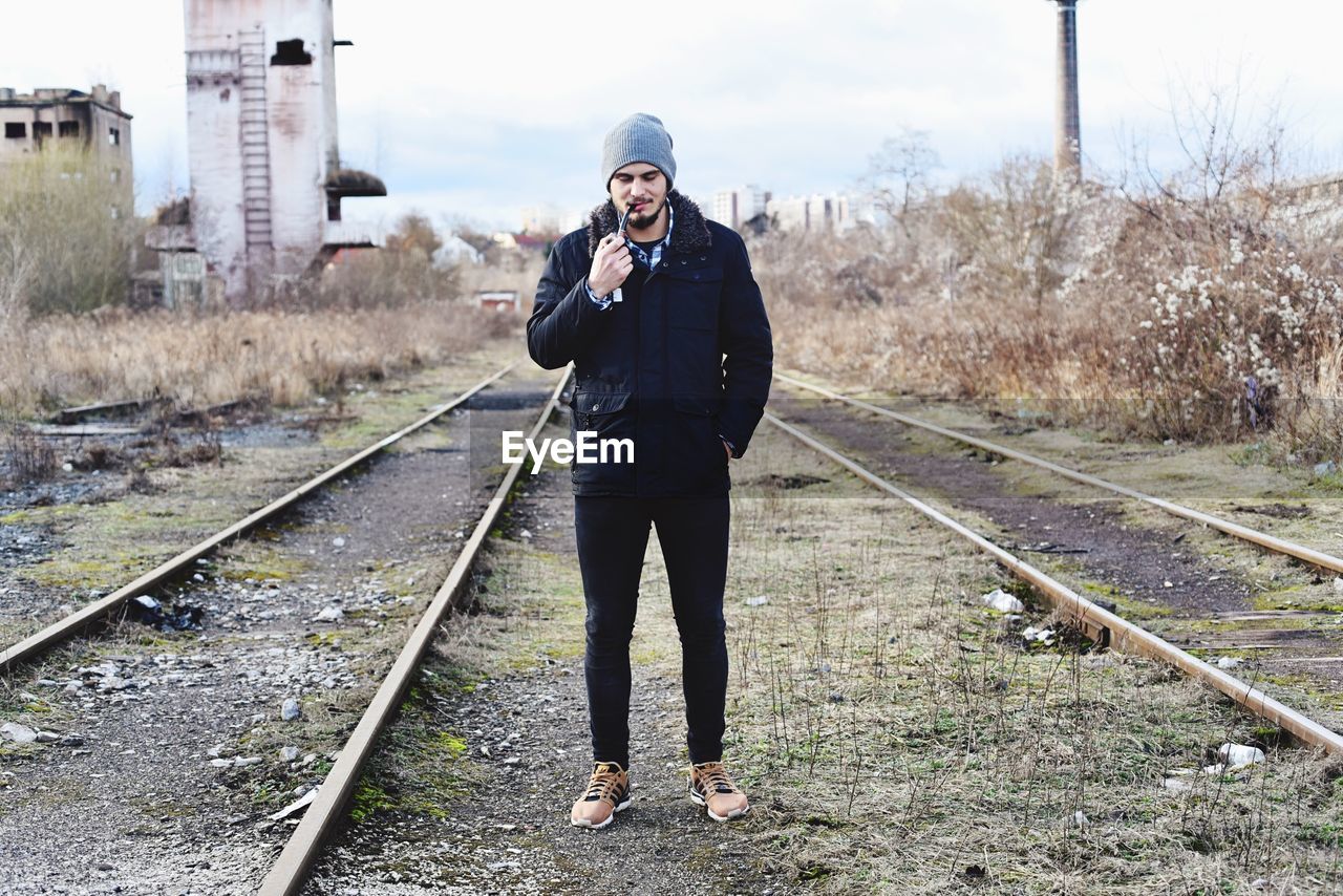 Full length of man smoking pipe at railroad track