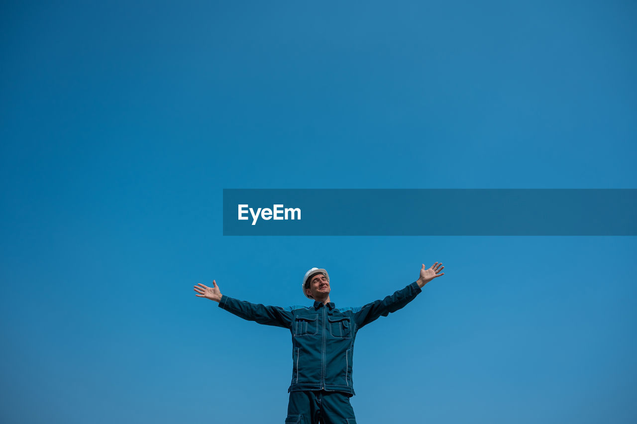 rear view of woman with arms raised against clear blue sky