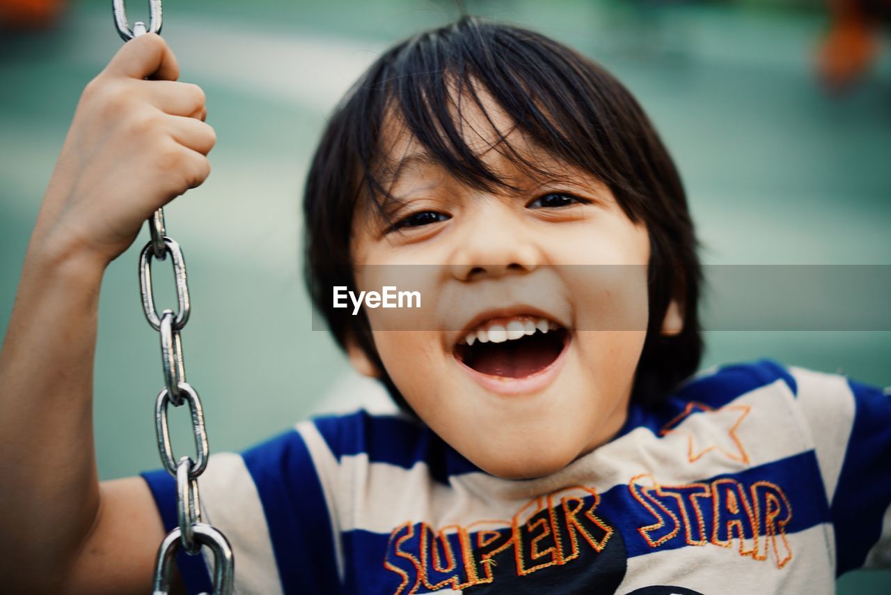 Close-up portrait of smiling boy swinging in playground