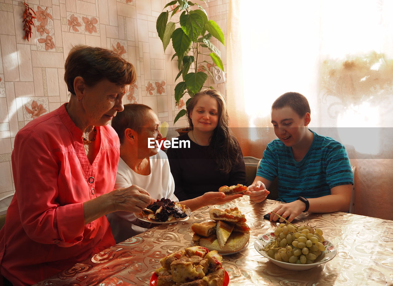 An elderly woman in bright clothes sets the table, arranges homemade cakes, prepares 