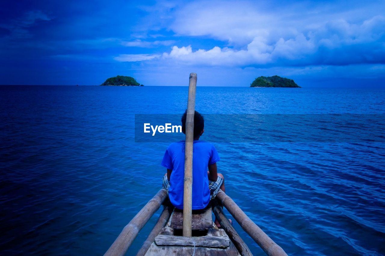 Rear view of boy on boat at sea against sky during dusk