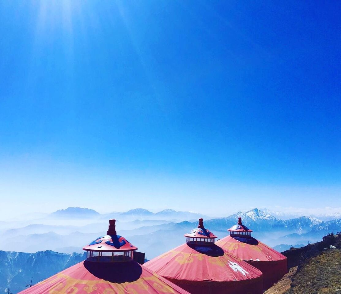 Built structures by mountains against clear blue sky on sunny day