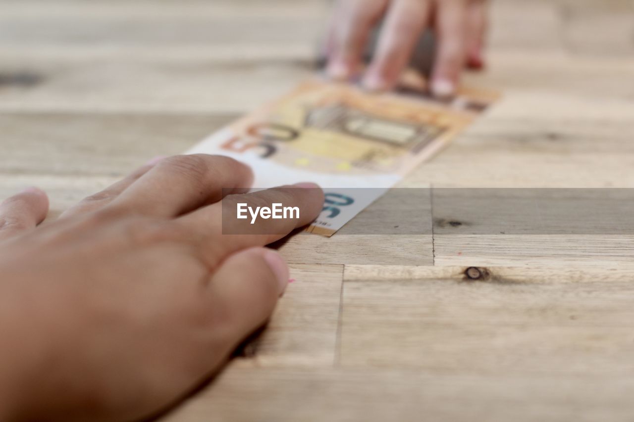 Cropped hand of person giving paper currency 50 euro to a child on table