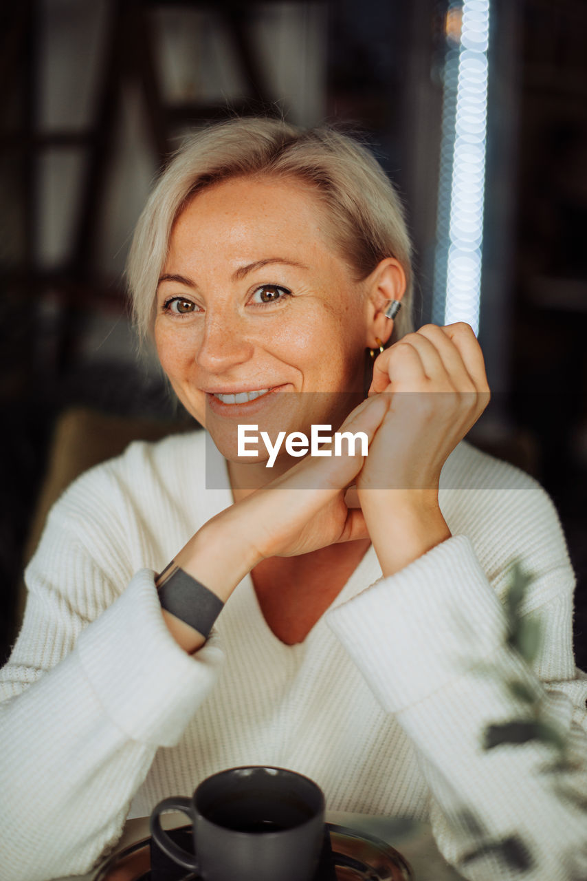 Blond caucasian woman smiling at camera while sitting at table