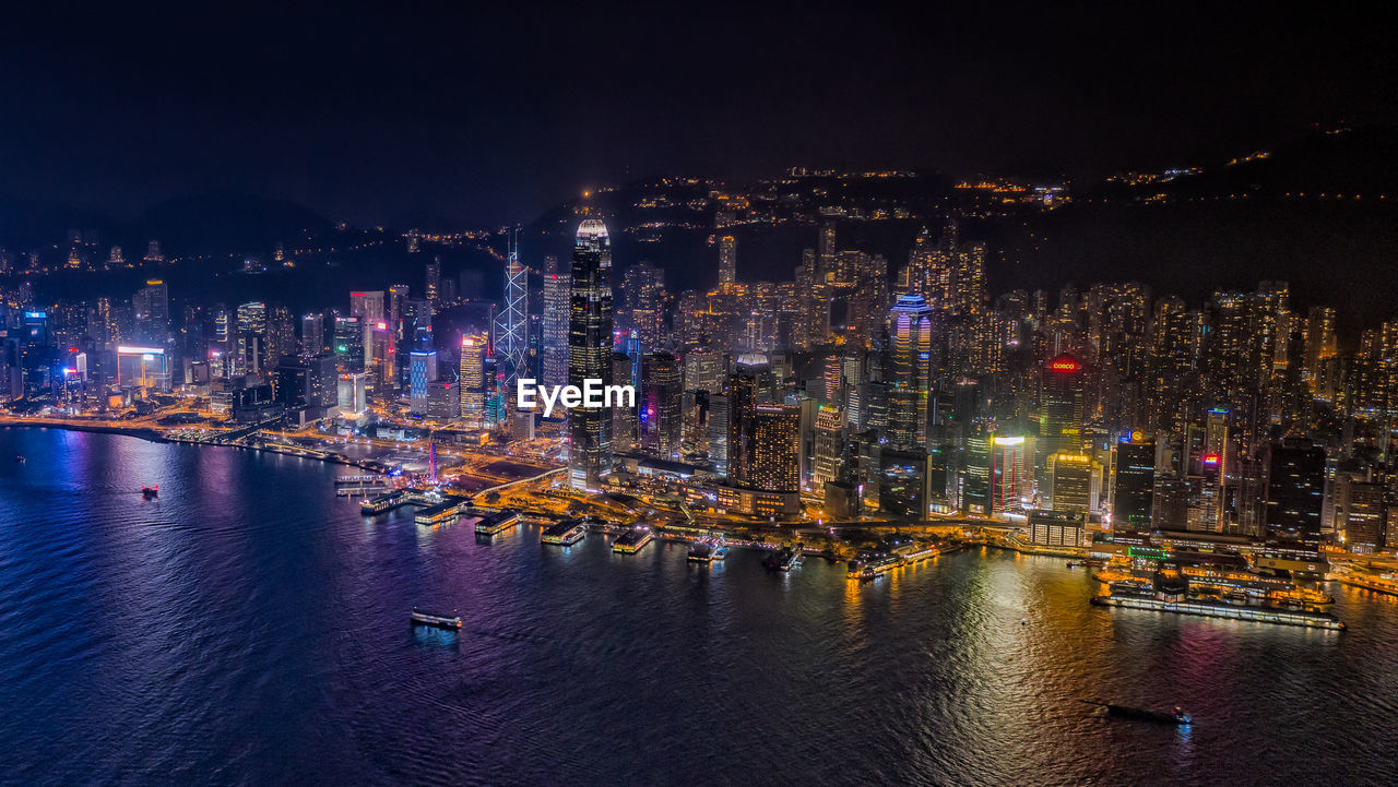 Illuminated buildings by river against sky at night