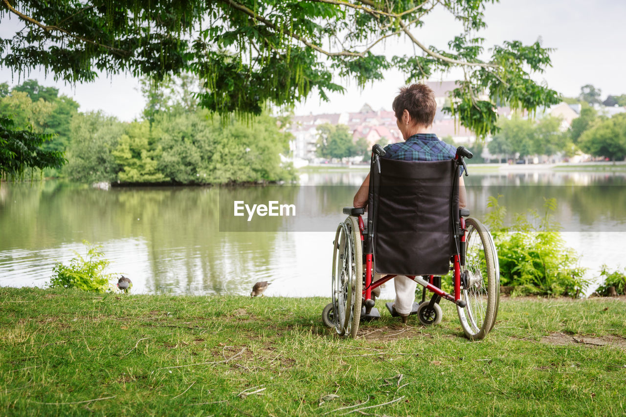 Woman sitting on wheelchair by lake in public park