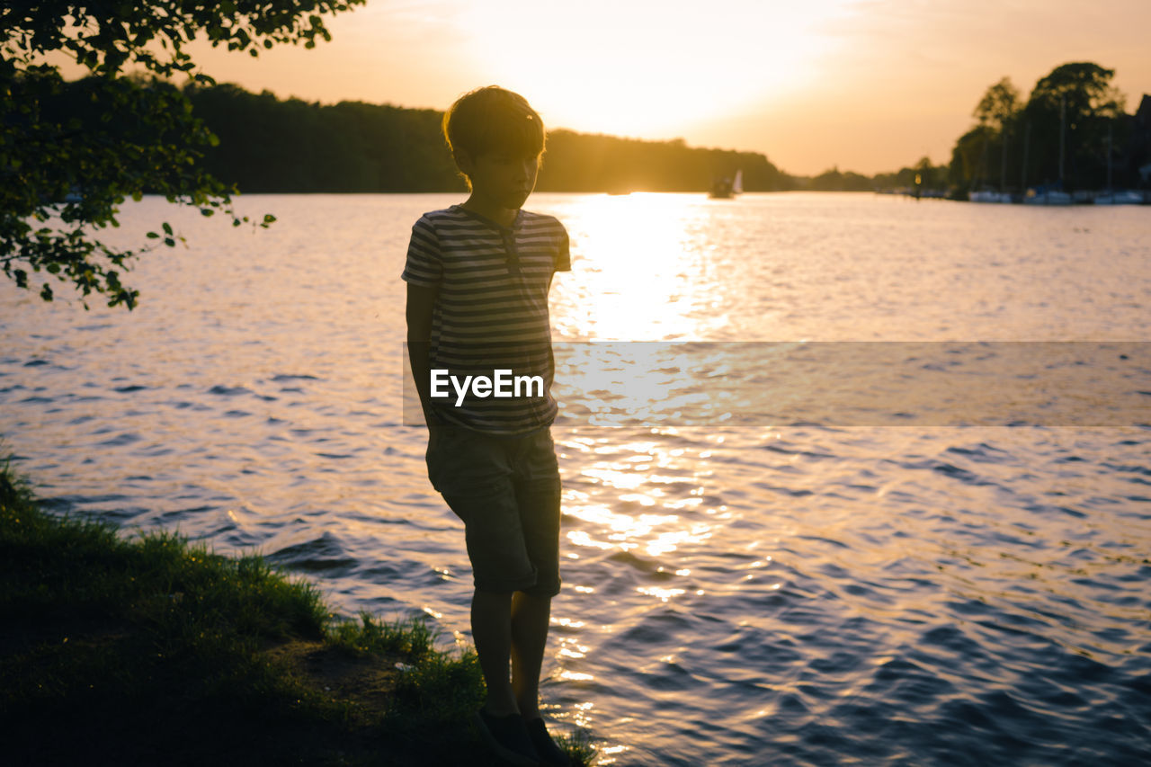 Boy standing by lake during sunset