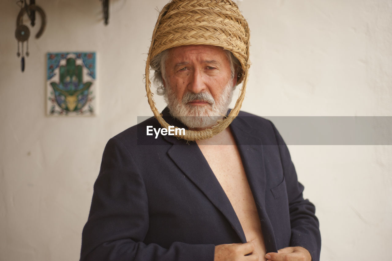 Portrait of man wearing basket on head while standing against wall