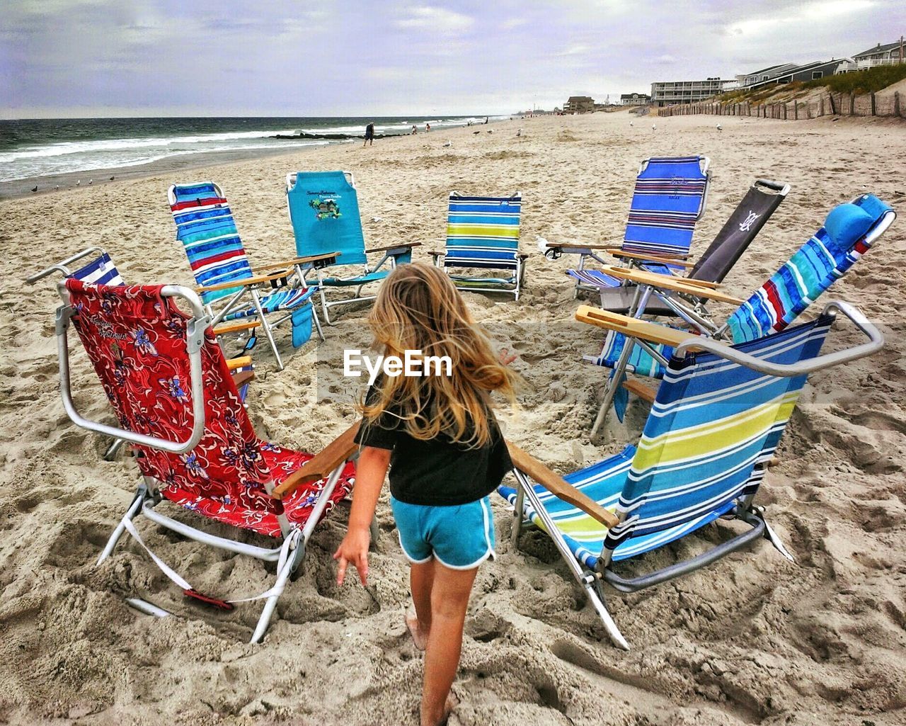 High angle view of girl on sandy beach amidst deck chairs