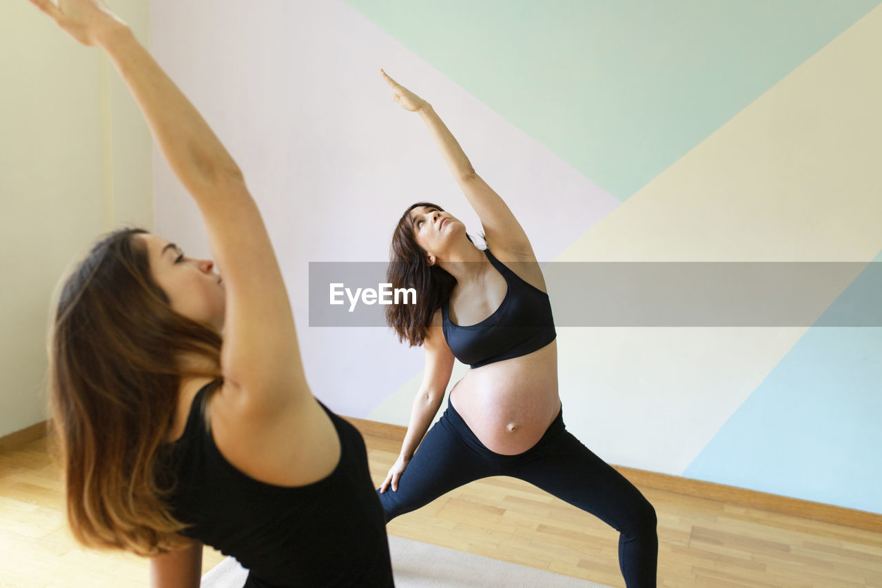 Pregnant woman exercising with instructor in yoga studio