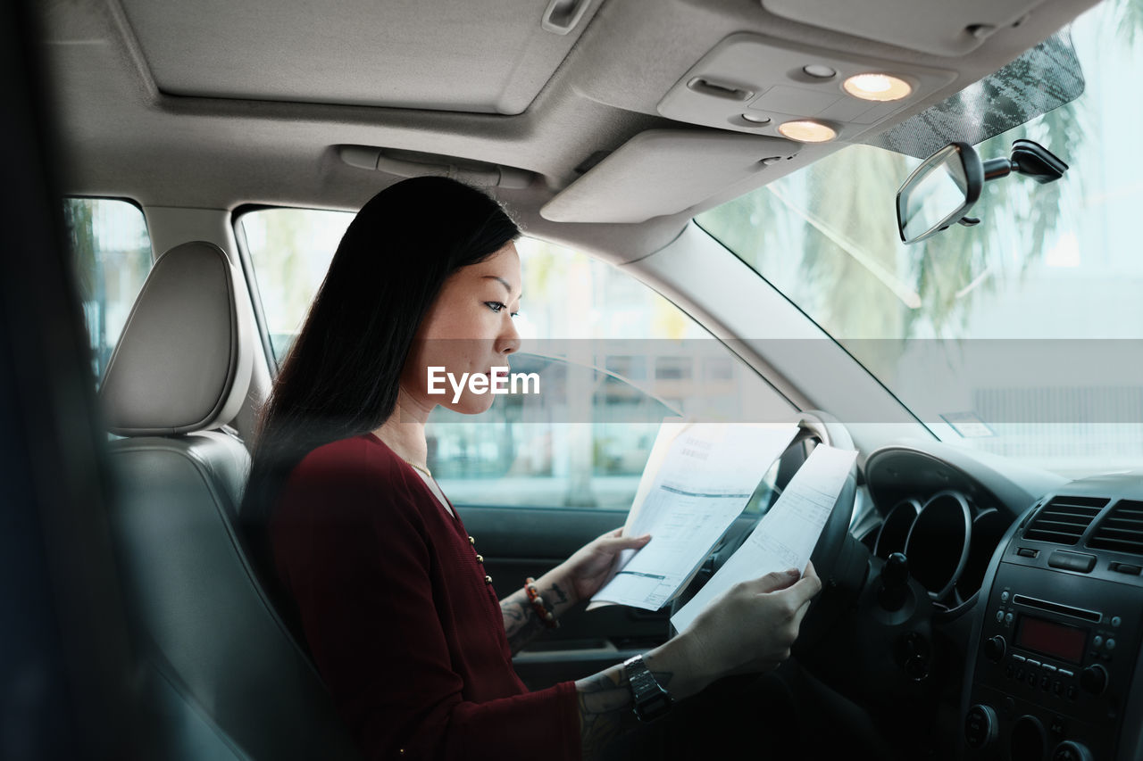 Side view of woman holding documents while sitting in car