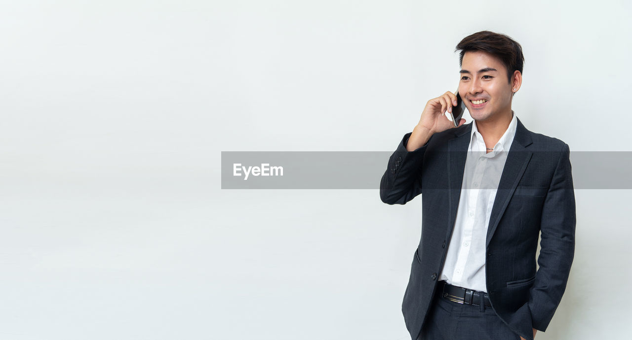 PORTRAIT OF SMILING MAN STANDING AGAINST WHITE BACKGROUND