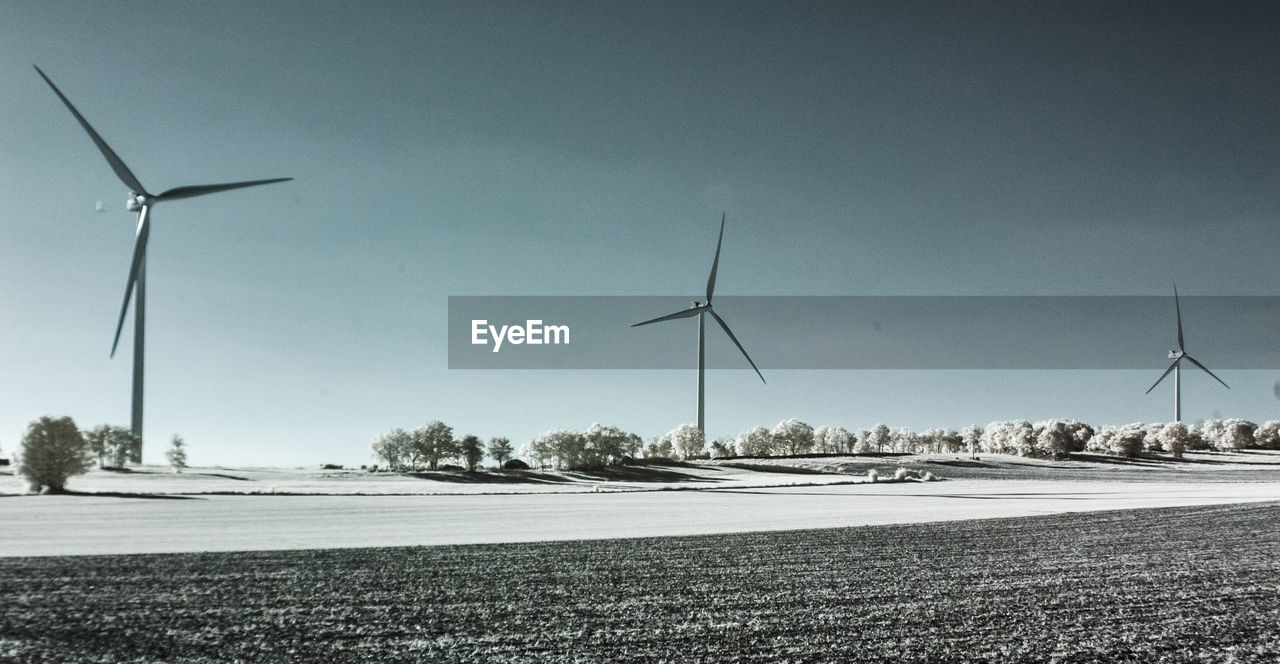 WINDMILLS ON FIELD AGAINST SKY
