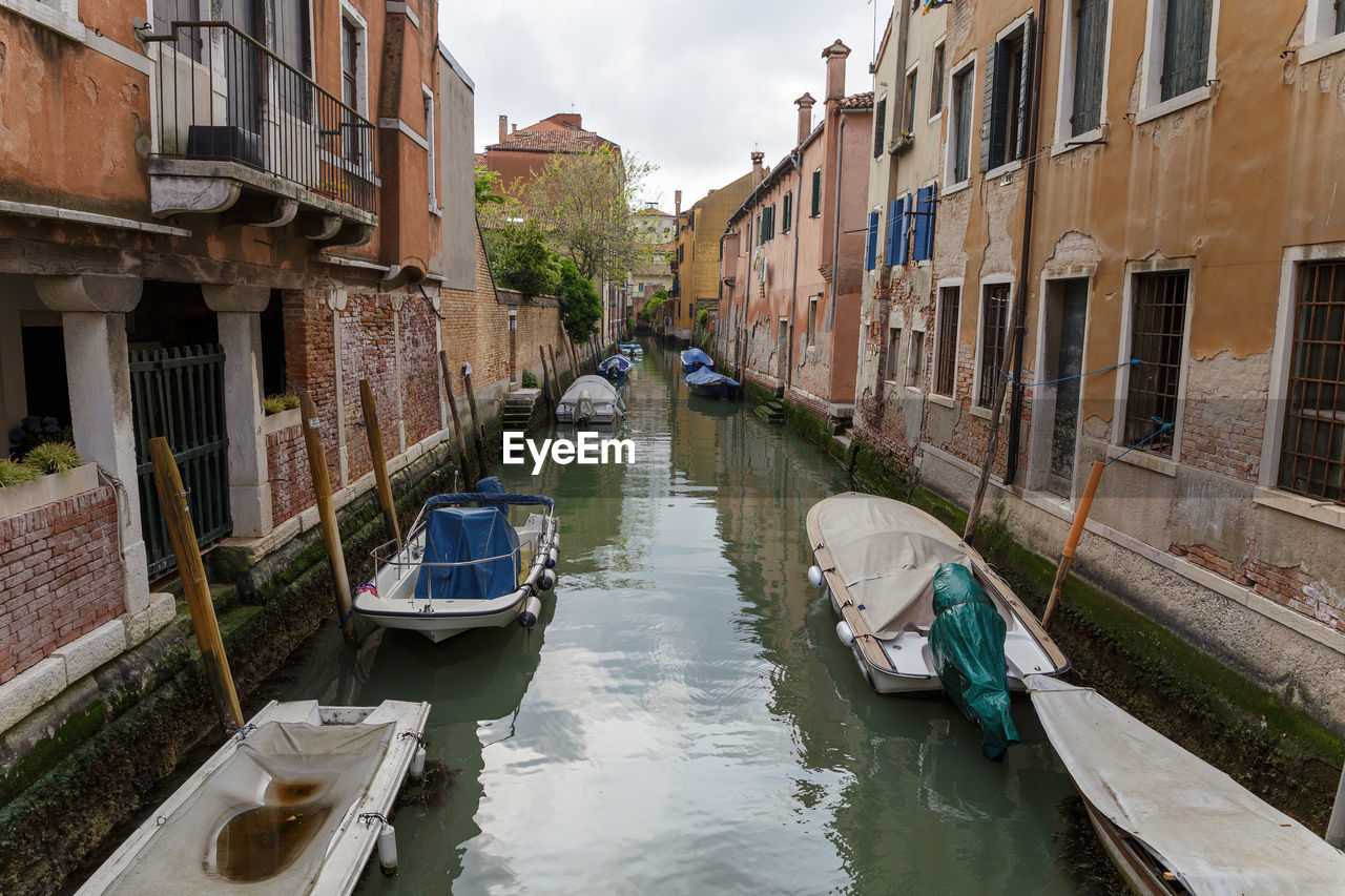 BOATS MOORED IN CANAL AMIDST BUILDINGS AGAINST SKY