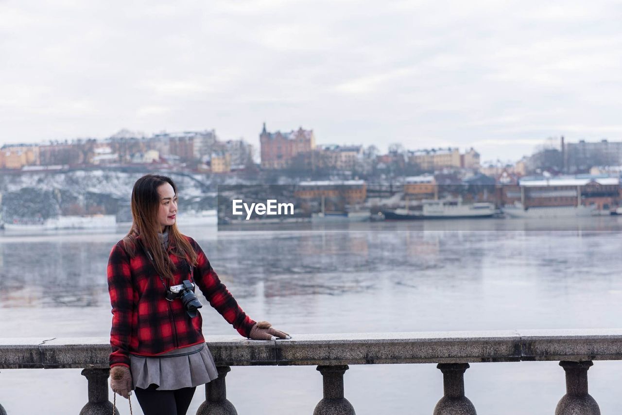 Woman standing by railing against river in city