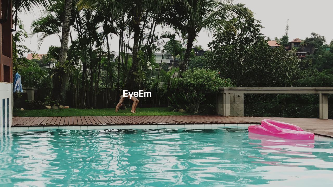 MAN SWIMMING IN POOL AGAINST TREES AND SKY