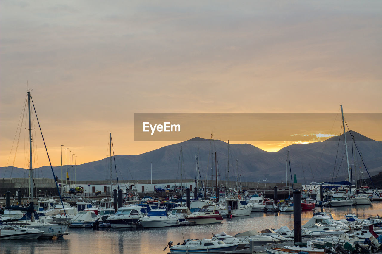 Boats moored in harbor at sunset