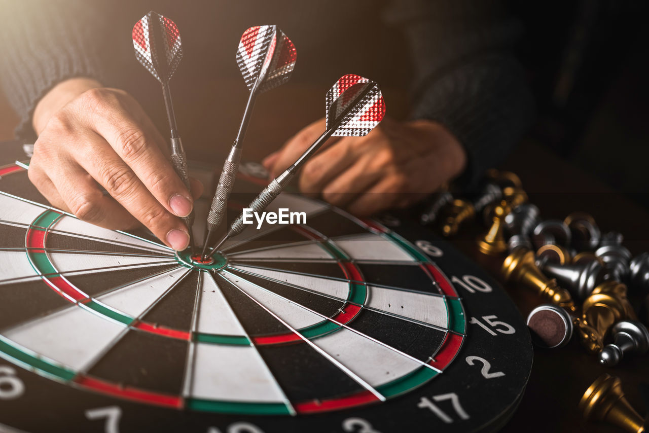 Midsection of person holding dart on dartboard