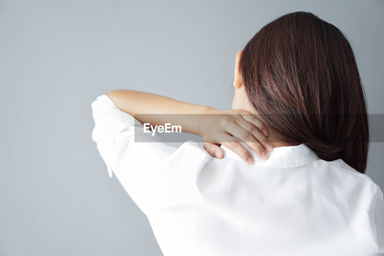 Rear view of woman having neckache against gray background