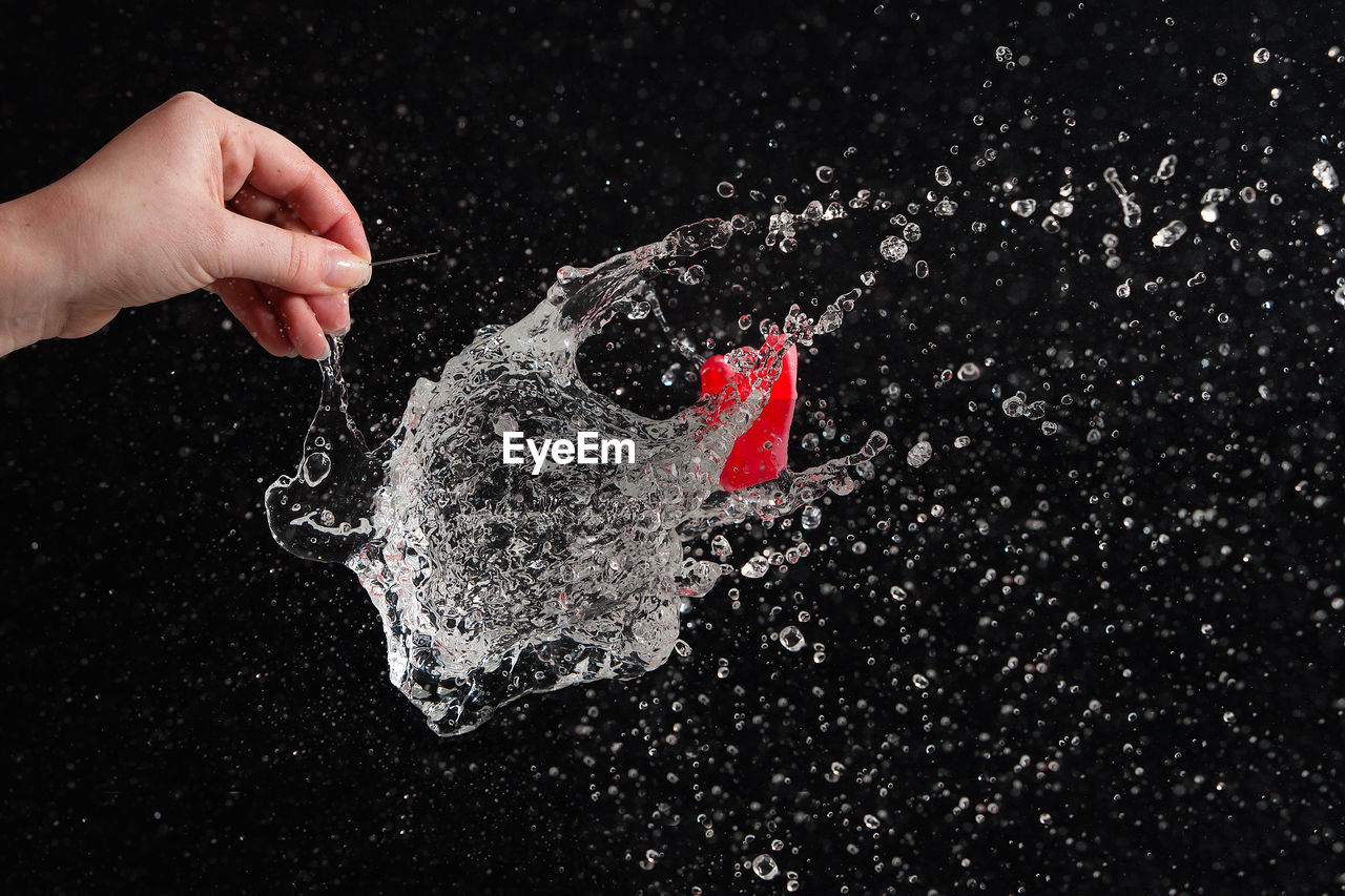 Cropped hand of person exploding water bomb against black background