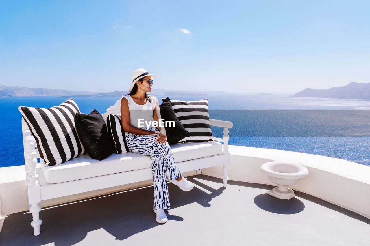 Young woman sitting on sofa at terrace against sea