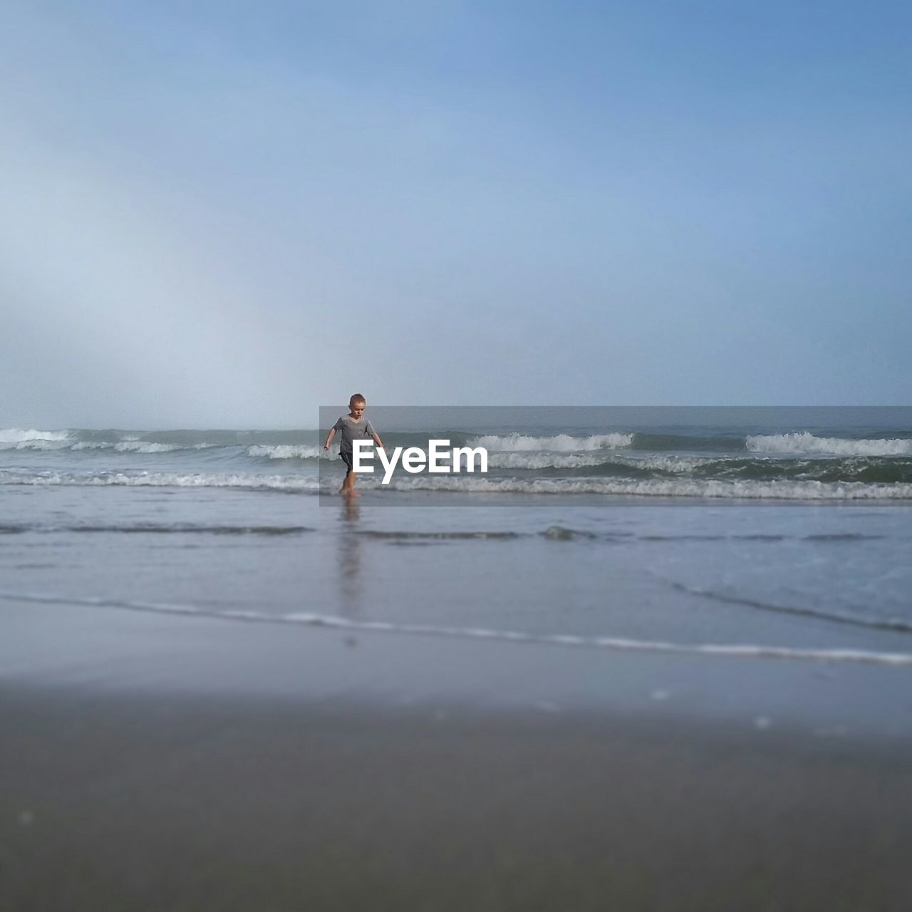 Boy walking on beach against clear sky