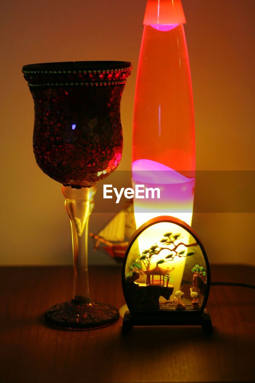 CLOSE-UP OF WINE GLASSES ON TABLE AGAINST ILLUMINATED LAMP