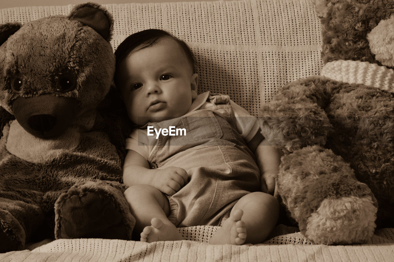 Baby boy sitting by teddy bears on sofa