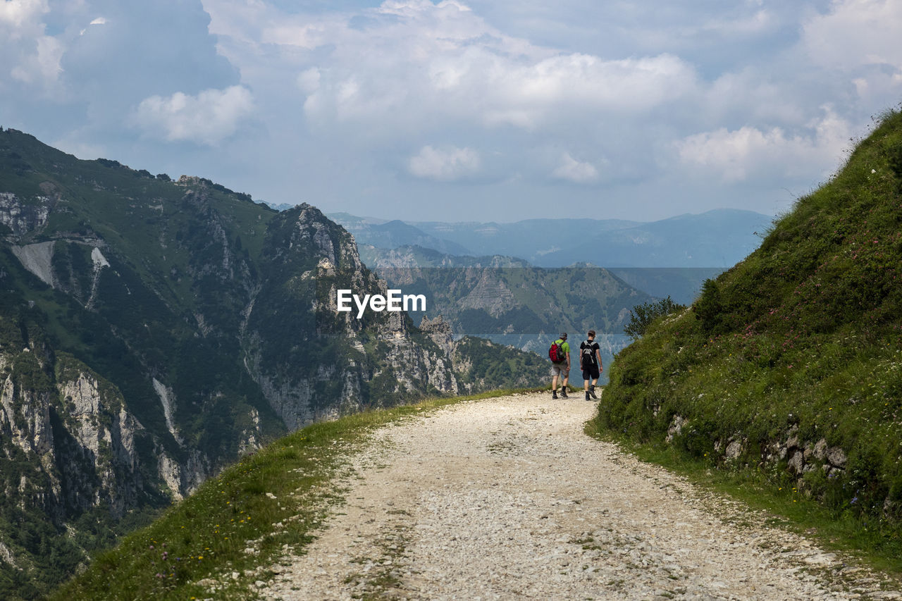 Rear view of people walking on road amidst mountains against sky