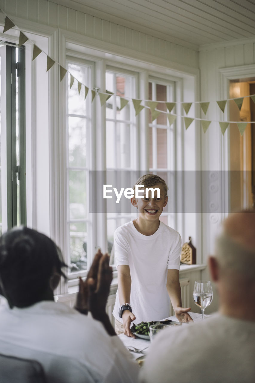 Smiling boy serving food during dinner party at home