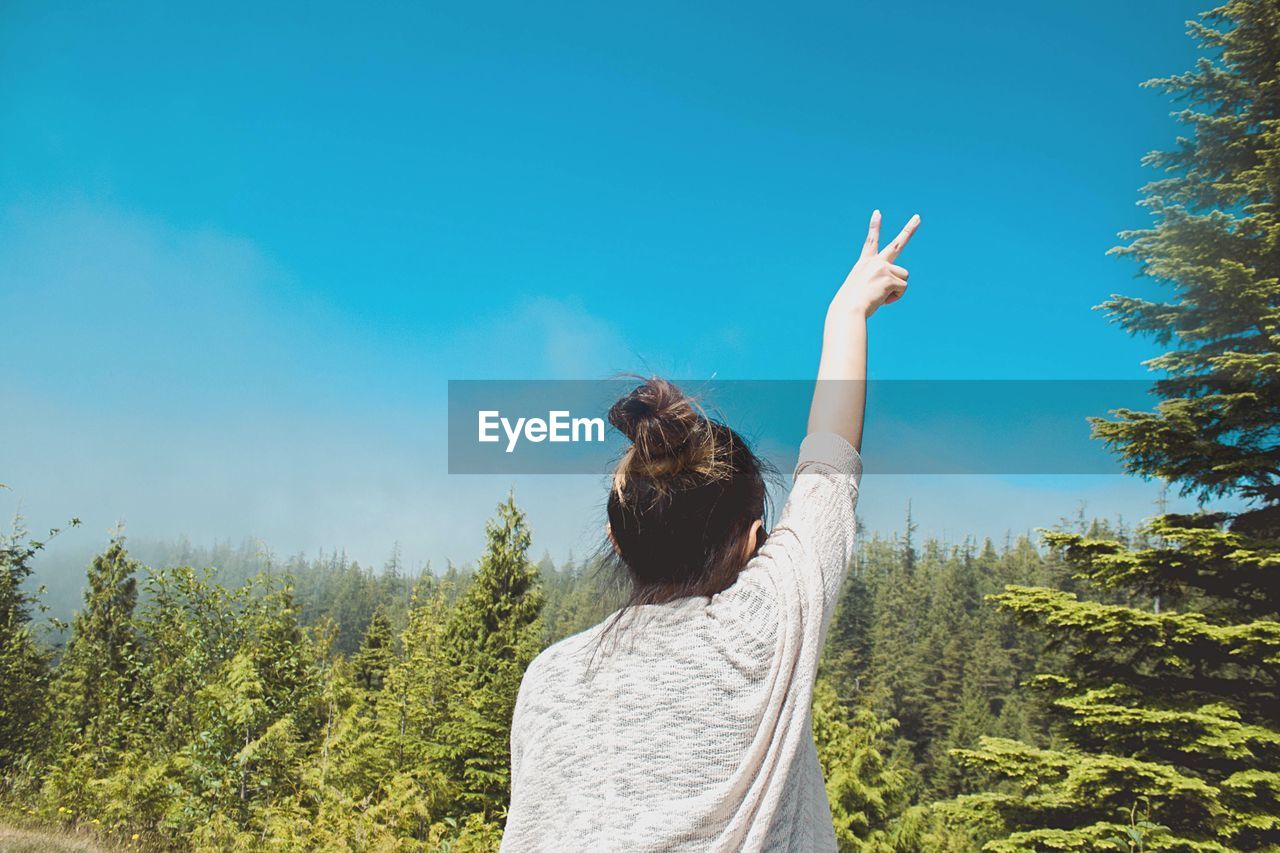 Rear view of woman with peace sign against blue sky